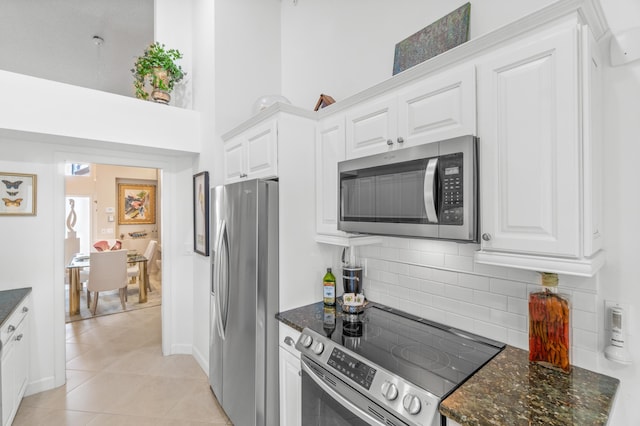 kitchen featuring backsplash, dark stone counters, stainless steel appliances, light tile patterned floors, and white cabinetry