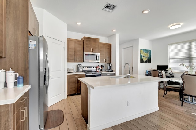 kitchen featuring light hardwood / wood-style floors, sink, stainless steel appliances, and an island with sink