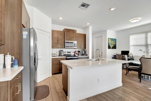 kitchen featuring stainless steel dishwasher, dark brown cabinets, a kitchen island with sink, sink, and light hardwood / wood-style flooring