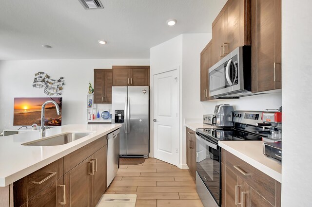 kitchen with appliances with stainless steel finishes, light wood-type flooring, an island with sink, and sink