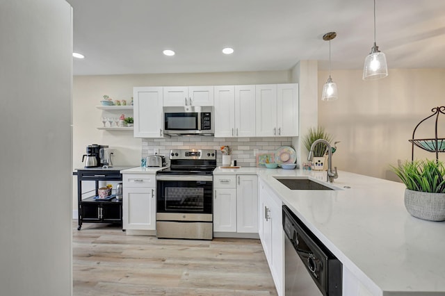 kitchen with sink, hanging light fixtures, appliances with stainless steel finishes, white cabinets, and backsplash