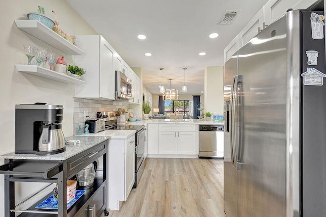 kitchen with hanging light fixtures, light wood-type flooring, stainless steel appliances, decorative backsplash, and white cabinets