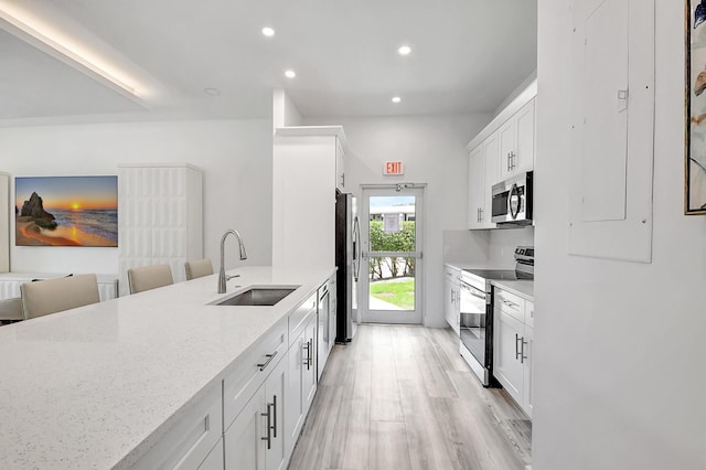 kitchen with white cabinetry, stainless steel appliances, light stone countertops, and sink