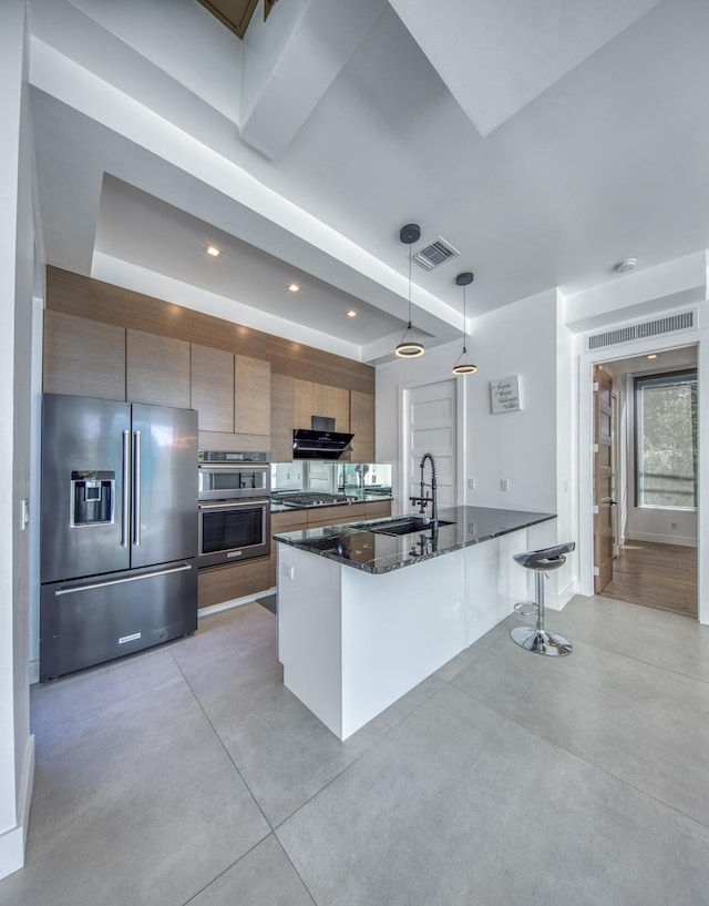 kitchen with sink, stainless steel appliances, ventilation hood, dark stone countertops, and pendant lighting