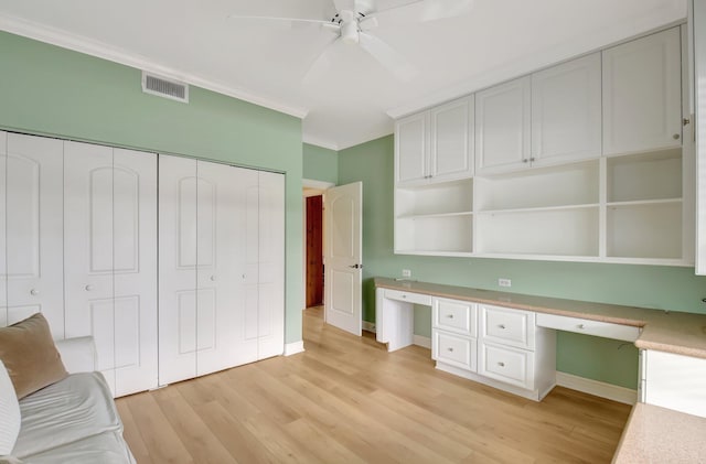 unfurnished office featuring ceiling fan, ornamental molding, built in desk, and light hardwood / wood-style floors