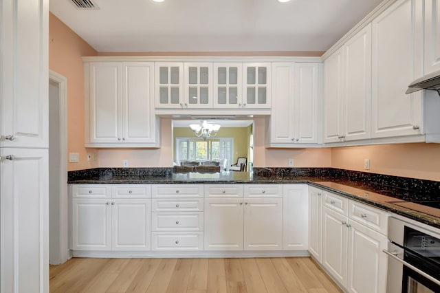 kitchen with white cabinets, light hardwood / wood-style flooring, dark stone countertops, and stainless steel oven