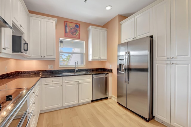 kitchen featuring appliances with stainless steel finishes, light wood-type flooring, sink, dark stone countertops, and white cabinets