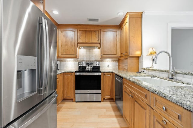 kitchen with sink, stainless steel appliances, light stone counters, premium range hood, and light wood-type flooring