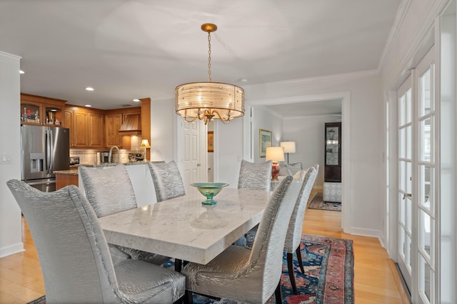 dining area featuring light hardwood / wood-style floors, a notable chandelier, crown molding, and sink