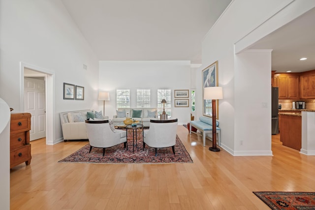 living room featuring light wood-type flooring, crown molding, and a high ceiling