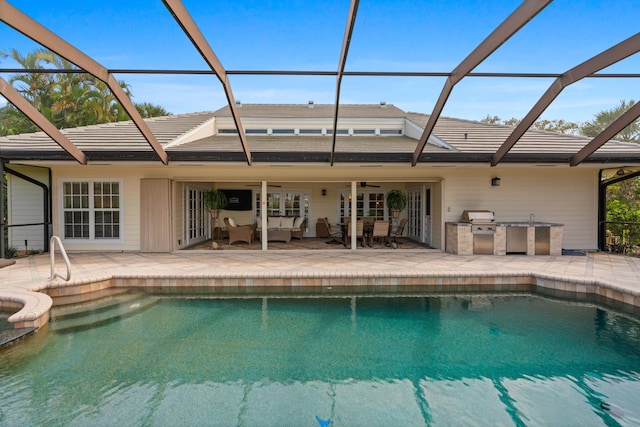 view of pool featuring glass enclosure, ceiling fan, a patio area, an outdoor kitchen, and area for grilling