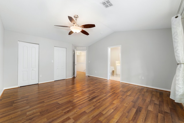 unfurnished bedroom featuring ensuite bathroom, vaulted ceiling, ceiling fan, dark hardwood / wood-style floors, and multiple closets