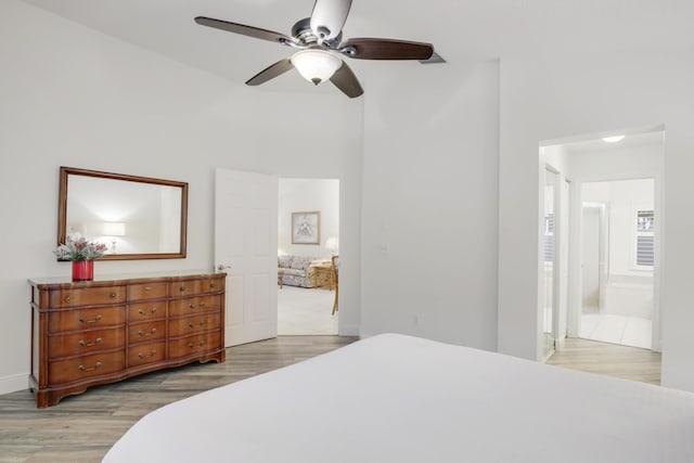 bedroom featuring baseboards, ensuite bath, a ceiling fan, and light wood-style floors