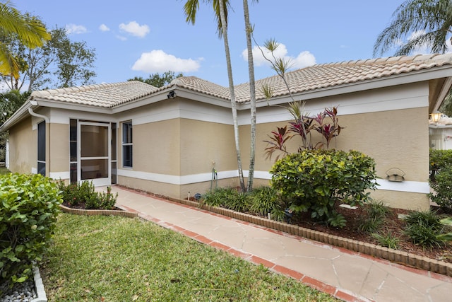 view of property exterior featuring a tile roof, a lawn, and stucco siding