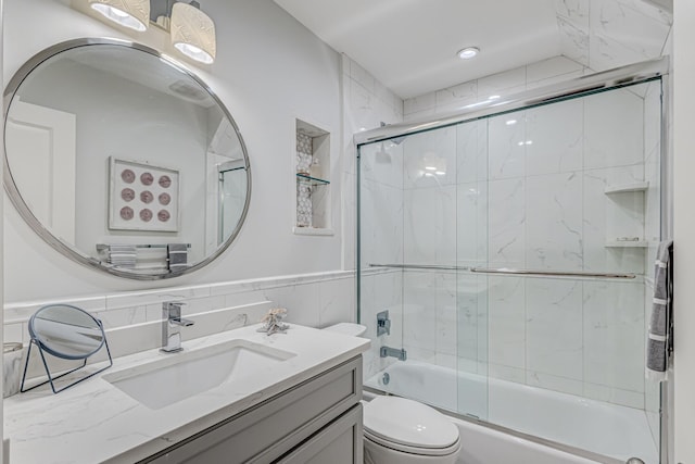 full bathroom featuring vanity, toilet, tile walls, and enclosed tub / shower combo