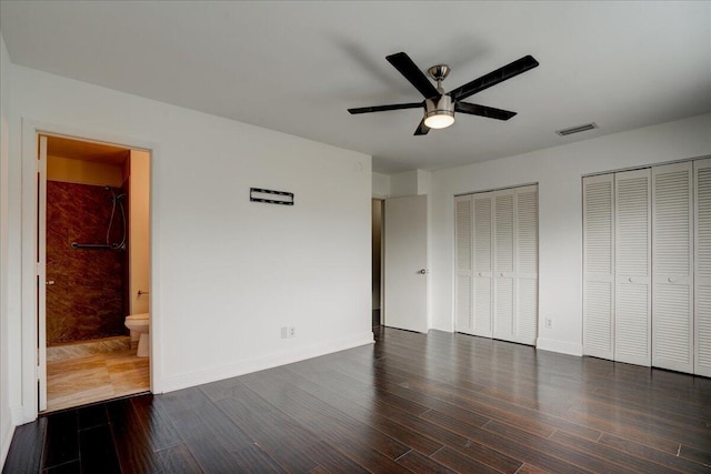 unfurnished bedroom with ceiling fan, two closets, dark hardwood / wood-style flooring, and ensuite bath