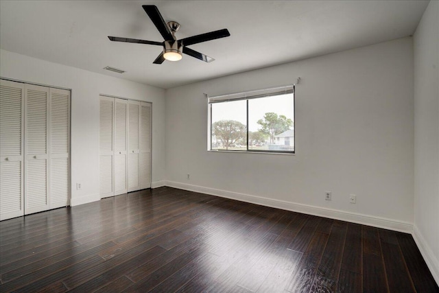 unfurnished bedroom featuring ceiling fan, dark hardwood / wood-style flooring, and two closets