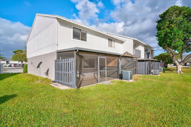 back of property with central air condition unit, a sunroom, and a lawn