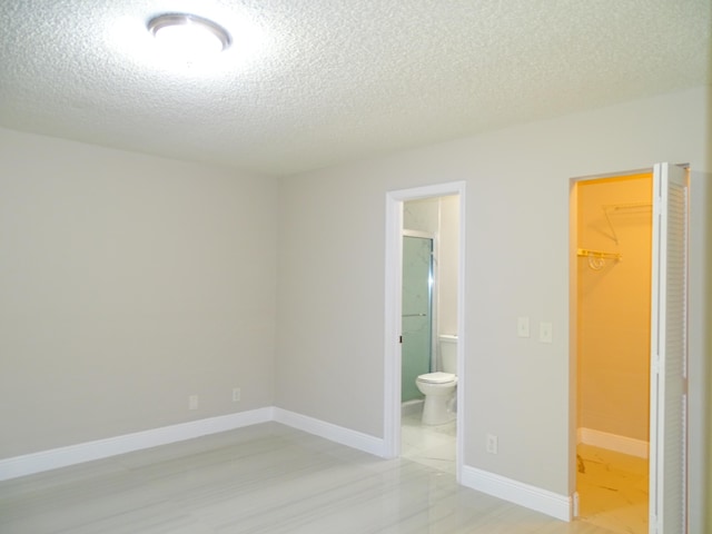 unfurnished bedroom with a textured ceiling, a walk in closet, ensuite bath, and a closet