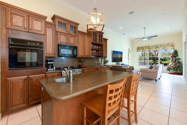 kitchen featuring light tile patterned floors, sink, a kitchen breakfast bar, black appliances, and a center island with sink