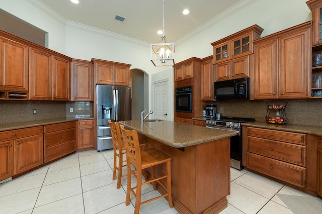 kitchen with light tile patterned floors, ornamental molding, black appliances, and a center island with sink