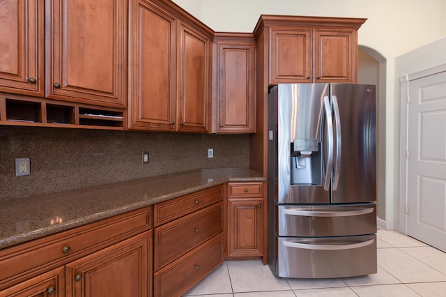 kitchen featuring dark stone countertops, decorative backsplash, light tile patterned floors, and stainless steel refrigerator with ice dispenser