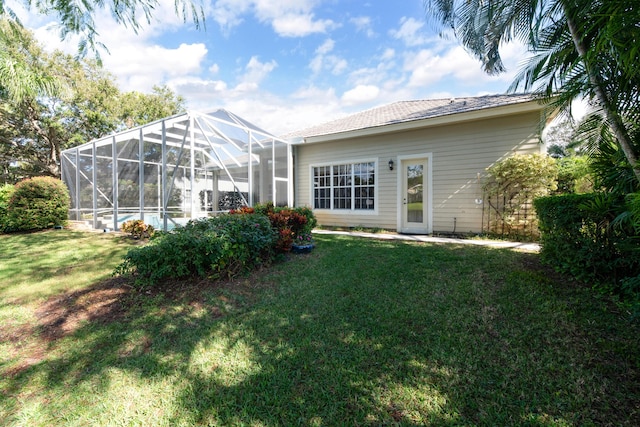 rear view of property with glass enclosure and a lawn