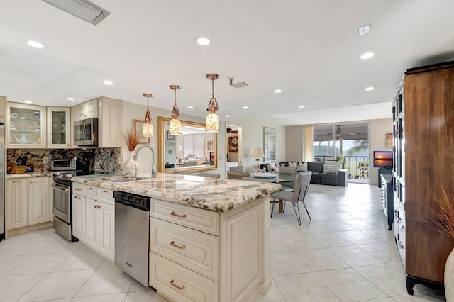 kitchen featuring tasteful backsplash, light stone counters, stainless steel appliances, sink, and pendant lighting