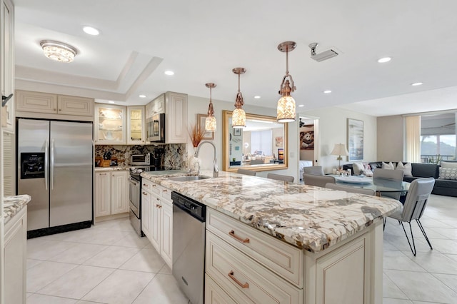 kitchen with light stone countertops, decorative light fixtures, stainless steel appliances, and cream cabinets