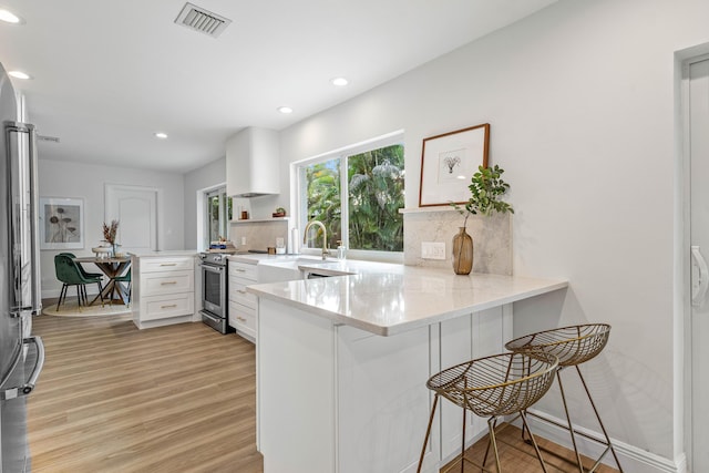 kitchen with tasteful backsplash, visible vents, gas range, a peninsula, and light wood-type flooring