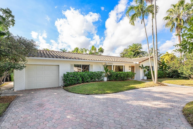 ranch-style house featuring brick siding, a tile roof, an attached garage, decorative driveway, and a front yard