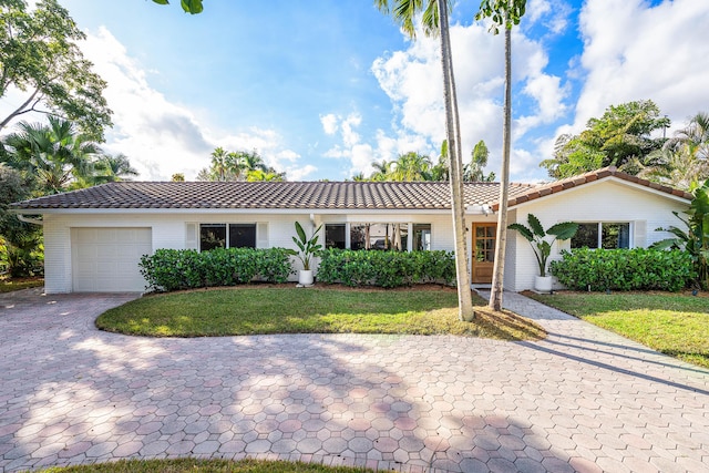 ranch-style house with a garage, a tiled roof, decorative driveway, a front yard, and brick siding