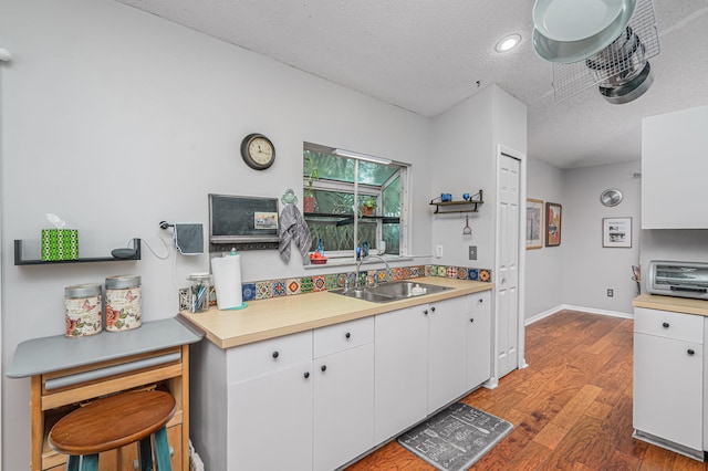 kitchen featuring a textured ceiling, wood-type flooring, white cabinetry, and sink