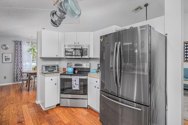 kitchen with a textured ceiling, light wood-type flooring, white cabinetry, and stainless steel appliances