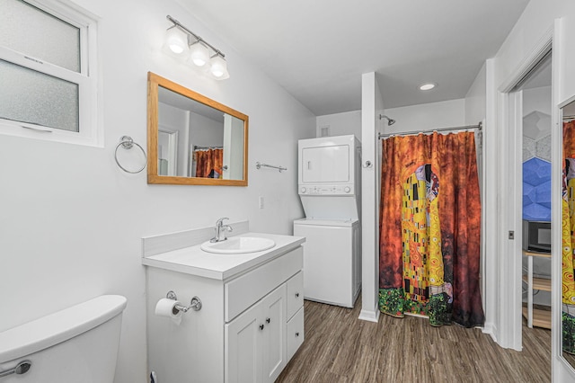 bathroom featuring walk in shower, stacked washer / dryer, toilet, vanity, and hardwood / wood-style flooring