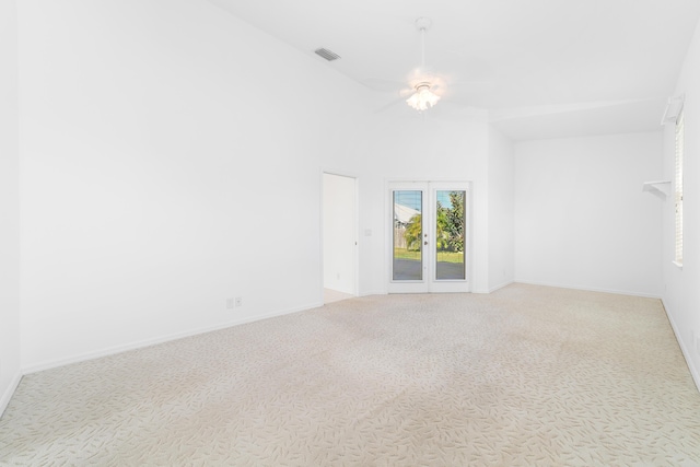 carpeted spare room with ceiling fan, high vaulted ceiling, and french doors