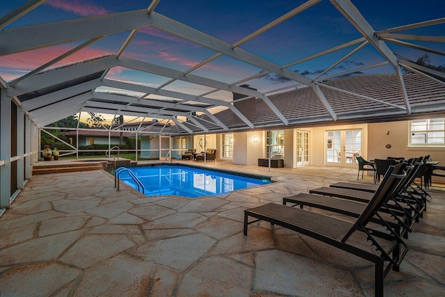 pool at dusk with french doors, a patio, and a lanai