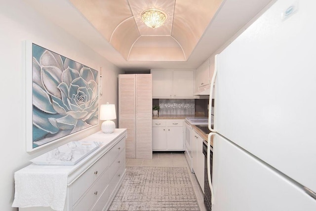 kitchen with white cabinetry, white refrigerator, a tray ceiling, decorative backsplash, and light tile patterned floors