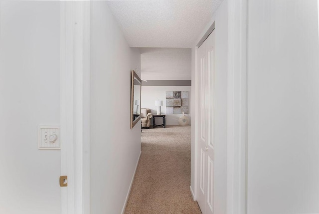 hallway with light colored carpet and a textured ceiling