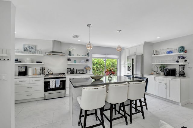 kitchen with sink, appliances with stainless steel finishes, pendant lighting, wall chimney range hood, and white cabinets