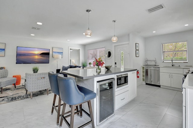 kitchen featuring a kitchen island, pendant lighting, white cabinets, beverage cooler, and stainless steel appliances