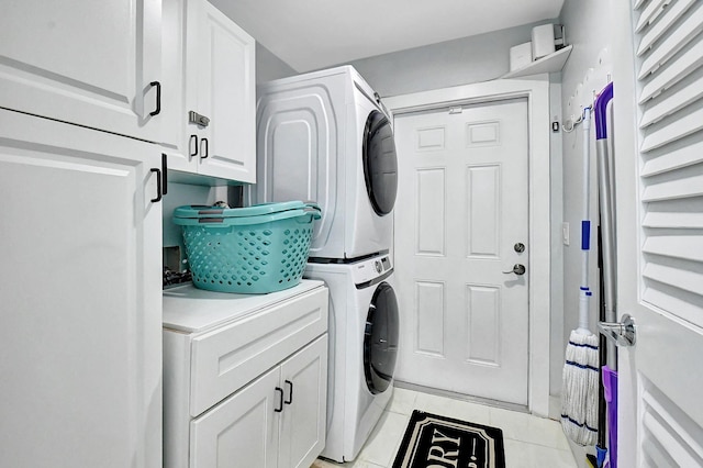 clothes washing area featuring cabinets, light tile patterned flooring, and stacked washer and clothes dryer