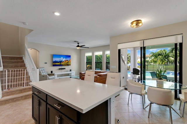 kitchen with dark brown cabinets, a center island, ceiling fan, and light tile patterned flooring