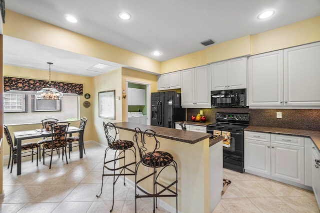 kitchen with white cabinetry, hanging light fixtures, washing machine and dryer, a breakfast bar area, and black appliances