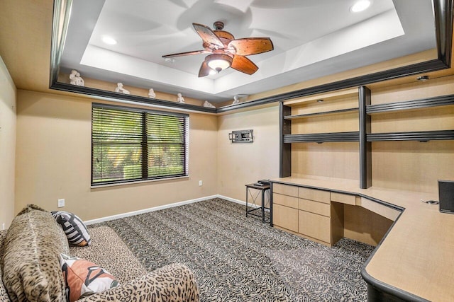 office space featuring dark carpet, a raised ceiling, and built in desk