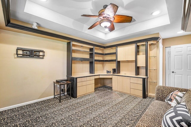 office featuring dark carpet, built in desk, a raised ceiling, and ceiling fan