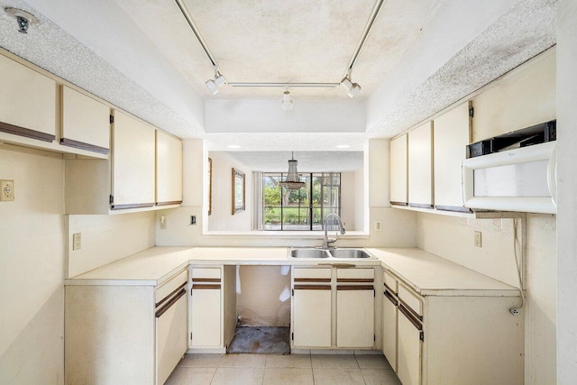 kitchen featuring rail lighting, sink, light tile patterned floors, a tray ceiling, and cream cabinets