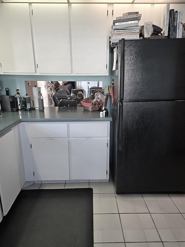 kitchen featuring black refrigerator, white cabinets, and light tile patterned flooring