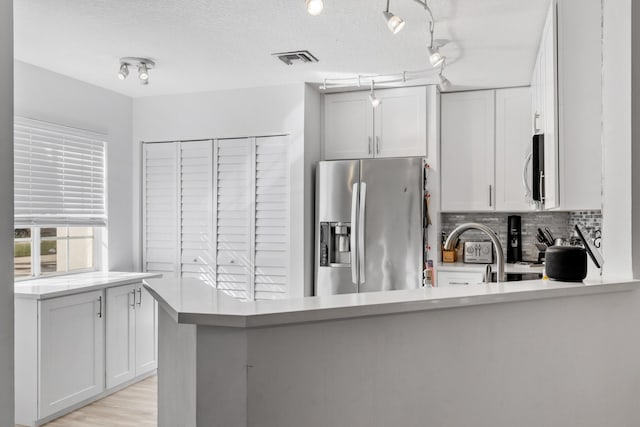 kitchen with kitchen peninsula, appliances with stainless steel finishes, backsplash, a textured ceiling, and white cabinetry