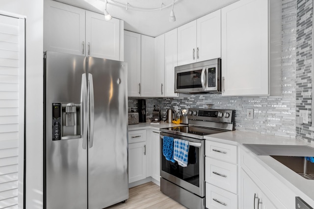 kitchen featuring backsplash, white cabinets, rail lighting, light hardwood / wood-style flooring, and appliances with stainless steel finishes